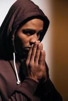 Full concentration. Confident young African man in hooded shirt keeping hands clasped near face and looking away photo