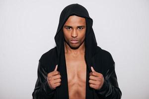 Cool and stylish. Confident young African man in hooded shirt looking at camera while standing against white background photo