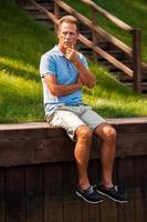 Finding a peaceful place to think. Thoughtful mature man holding hand on chin looking away while sitting at the quayside photo