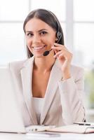 Supporting your business. Beautiful young businesswoman adjusting her headset and smiling while sitting at her working place photo