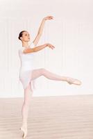 Grace and beauty in every move. Full length of beautiful young ballerina in white tutu dancing in ballet studio photo