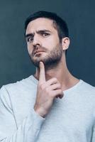 No way Frustrated young man touching his chin with finger and looking at camera while standing against grey background photo