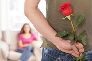 Flower for her. Cropped image of man holding a red rose while his girlfriend sitting on background photo