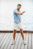 Keeping his body in tonus. Full length of handsome young man exercising while standing on quayside photo