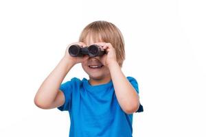 niño curioso. niño alegre mirando a través de binoculares y sonriendo mientras está de pie aislado en blanco foto