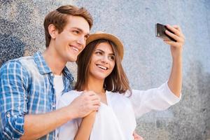 atrapar los momentos brillantes de la vida. hermosa joven pareja amorosa haciendo selfie con teléfono inteligente y sonriendo mientras se apoya en la pared foto