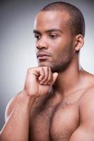 Handsome day dreamer. Portrait of young African man holding hand on chin and looking away while standing against black background photo