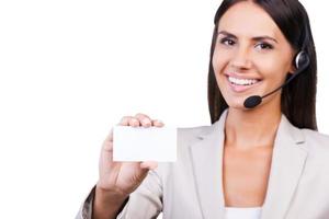 Call this number Beautiful young businesswoman in headset showing her business card and smiling while isolated on white background photo