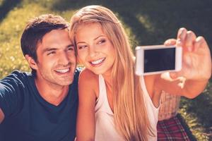 nos encanta selfie feliz joven pareja amorosa haciendo selfie y sonriendo mientras estamos sentados juntos en el césped en el parque foto