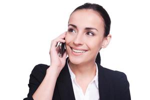 buena plática. Hermosa mujer joven en ropa formal hablando por teléfono móvil y sonriendo mientras está de pie aislado en blanco foto