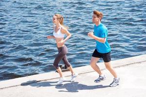 trotar juntos. vista superior de una mujer joven y un hombre con ropa deportiva corriendo a lo largo de la orilla del río foto