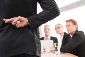 Lying Rear view of man in formalwear keeping fingers crossed behind his back while three people sitting on background photo