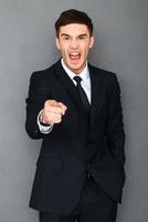 Go away Angry young man in formalwear pointing at camera and screaming while standing against grey background photo