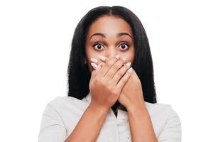 Unbelievable news Shocked young African woman covering mouth with hands and looking at camera while standing against white background photo