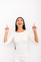 Look over there Cheerful young woman pointing up while standing against white background photo