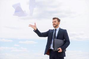 Tired of paperwork. Frustrated young businessman throwing documents away while standing against blue sky photo