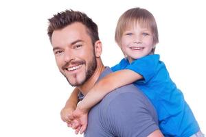 Piggyback ride. Side view of happy father carrying his son on back and smiling while both standing isolated on white photo