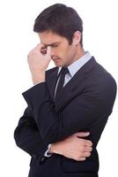 Lost in thoughts. Side view of frustrated young man in white shirt holding hand in hair and keeping eyes closed while standing isolated on white background photo