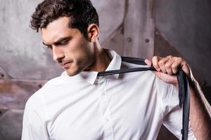 quitándole la corbata. joven cansado con ropa formal quitándose la corbata y mirando hacia otro lado foto