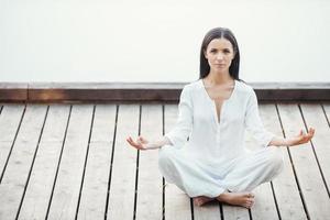 Yoga is my life. Beautiful young woman in white clothing meditating on seaside photo