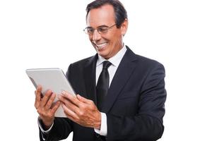 examinando su tableta nueva. hombre maduro confiado en ropa formal sosteniendo una tableta digital y mirándola con una sonrisa mientras está de pie aislado en fondo blanco