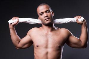 Confident in his perfect body. Young shirtless African man carrying towel on shoulders and looking at camera while standing against grey background photo