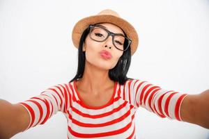Kiss me beautiful young woman making selfie on camera while standing against white background photo
