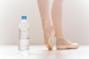 Water is important part of training. Close-up of bottle with water and legs of ballerina in the background photo