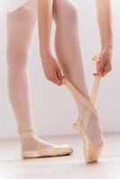 Preparing to dance. Close-up of ballerina tying her slippers while standing on hardwood floor photo