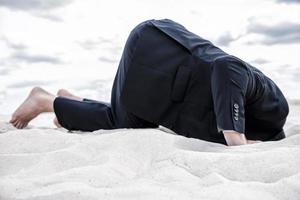 Hiding from his problems. Barefoot man in formalwear hiding his head in sand photo