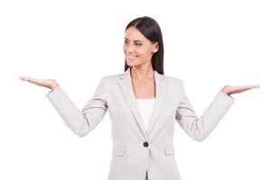 Hard choice. Beautiful young businesswoman in suit holding copy spaces in both hands and smiling while standing against white background photo