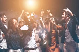 Party all night long. Group of beautiful young people dancing with champagne flutes and looking happy photo