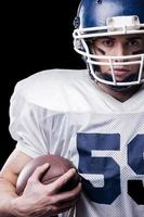 Leading this game  American football player looking at camera and holding ball while standing against black background photo