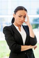 Feeling tired and overworked. Frustrated young woman in formalwear touching head with hand and touching face with hand while standing outdoors photo