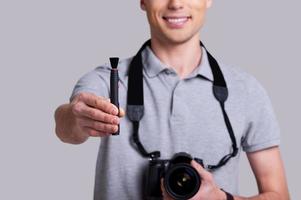 limpie la imagen recortada de su lente de un joven alegre con camisa de polo sosteniendo una cámara digital y estirando el cepillo de lentes mientras está de pie en el estudio foto