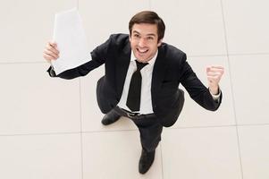 This contract is mine Top view of excited young man in formalwear holding a paper in one hand and gesturing photo