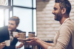 Your coffee to go Side view of barista passing coffee cups to his customer with smile while standing at bar counter photo