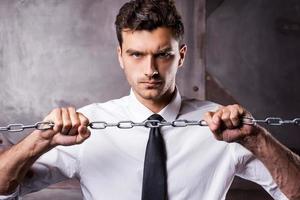 Trying to break a chain. Concentrated young man in shirt and tie trying to break a chain while looking at camera photo