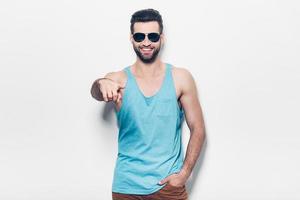 Choosing you. Confident young handsome man in sunglasses pointing you and smiling while standing against white background photo