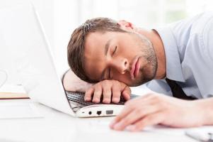 hombre de negocios durmiendo. vista lateral del joven con camisa y corbata durmiendo mientras está sentado en su lugar de trabajo foto