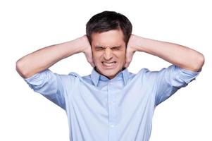 Too loud Handsome young man in blue shirt covering ears with hands and grimacing while standing isolated on white photo