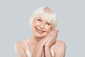Aging process. Beautiful senior woman looking at camera and smiling while standing against grey background photo