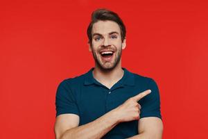 Portrait of happy young man in casual wear looking at camera and pointing away photo