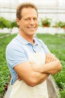 I have the best job in the world Handsome mature man in apron keeping arms crossed and smiling while standing in a greenhouse photo