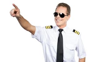 enamorado del cielo. piloto masculino confiado en uniforme apuntando hacia afuera y sonriendo mientras está de pie contra el fondo blanco foto
