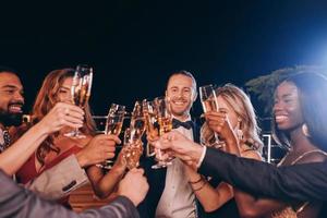 Group of people in formalwear toasting with champagne and smiling while spending time on luxury party photo