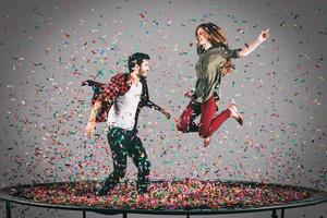 solo por diversión. toma en el aire de una hermosa pareja joven y alegre saltando en un trampolín junto con confetti a su alrededor foto