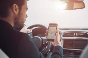 Checking the right way. Rear view of young man using smart phone to check the map while driving a car photo