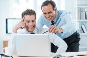 Lending him a hand with his work. Two cheerful business people in formalwear discussing something and looking at laptop photo