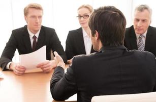 Telling about his work experience. Three people in formalwear interviewing young man sitting back to camera photo